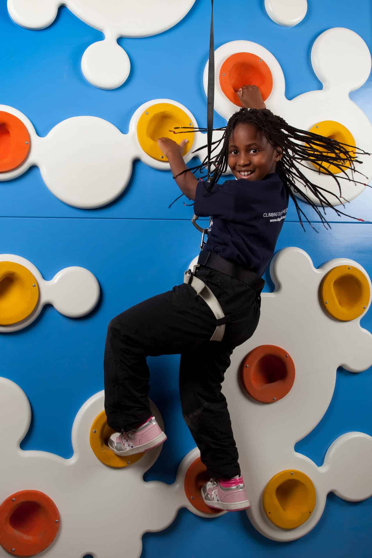 A young girl smiling and looking over her shoulder whilst climbing the Cloud 9 climbing wall